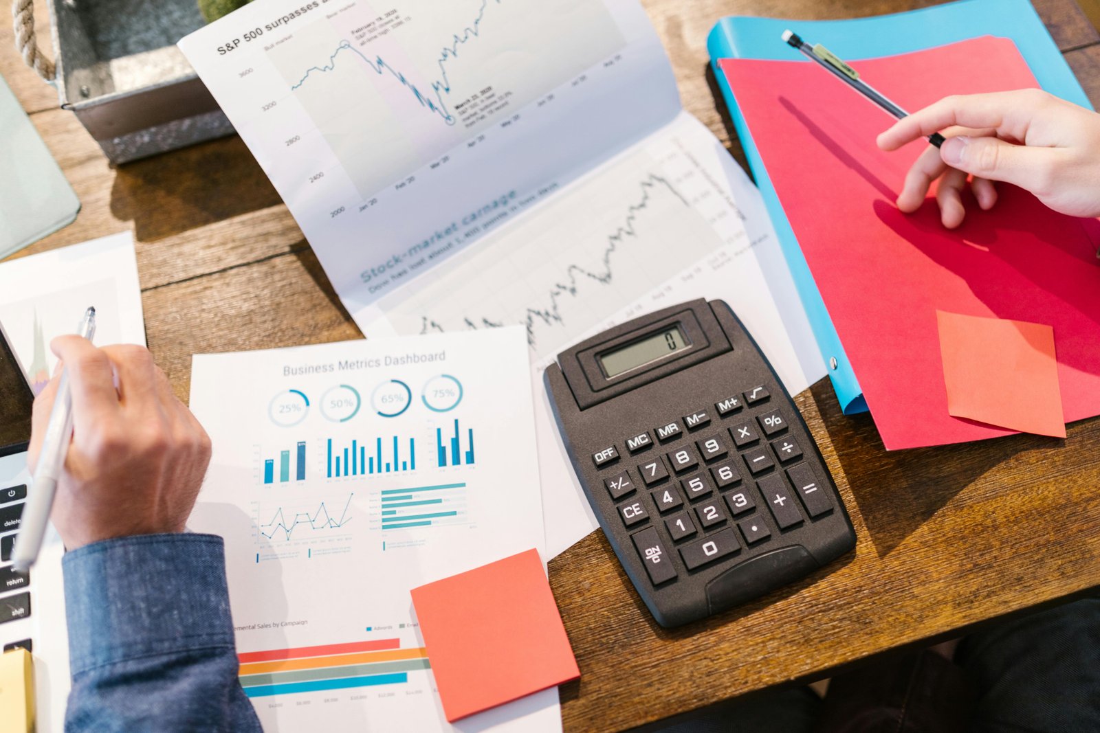 Close-up of a person's hands analyzing financial charts and documents with a calculator, emphasizing strategic use of free marketing tools.